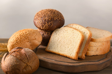 Variety of fresh tasty bread on wooden table against light background