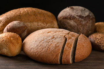 Variety of fresh tasty bread on wooden table against dark background