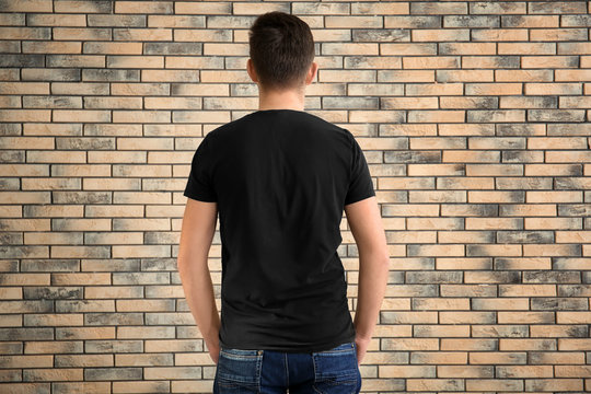 Young man in stylish t-shirt on brick wall background. Mockup for design
