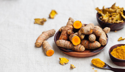 Fresh and dried turmeric roots in a wooden bowl. Grey textile background. Copy space.