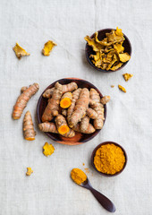 Fresh and dried turmeric roots in a wooden bowl. Grey textile background. Top view.