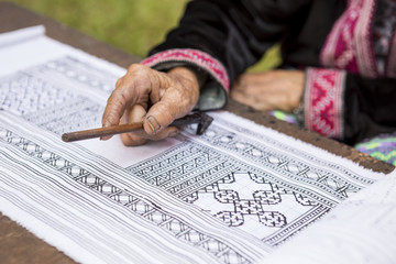Naklejka premium Old lady hand drawing pattern on white fabric with black hot wax, Thai style hilltribe handicraft, traditional style pattern