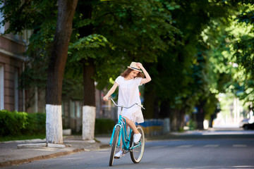 Young woman wearing a dress cycling in the city adjusting her hat copyspace countryside road trip journey happiness youth activity sportive vehicle transport.