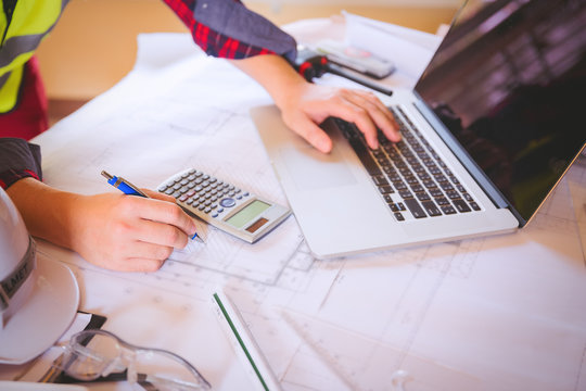Young asian man architect working on blueprint in the office,engineering work with blueprint,using calculator and laptop,teamwork,construction concept.