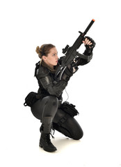 full length portrait of female wearing black  tactical armour, crouching pose holding a weapon, isolated on white studio background.