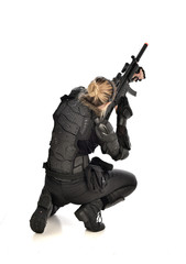 full length portrait of female wearing black  tactical armour, crouching pose holding a weapon, isolated on white studio background.