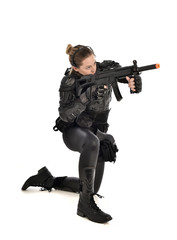 full length portrait of female wearing black  tactical armour, crouching pose holding a weapon, isolated on white studio background.