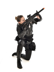 full length portrait of female wearing black  tactical armour, crouching pose holding a weapon, isolated on white studio background.