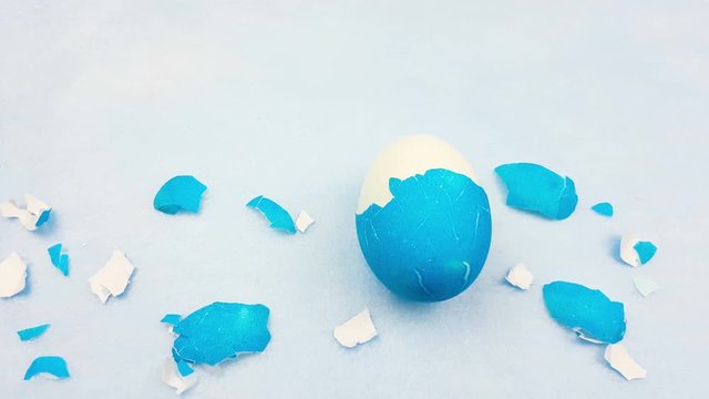 Eggshell with color easter egg on pastel blue background.