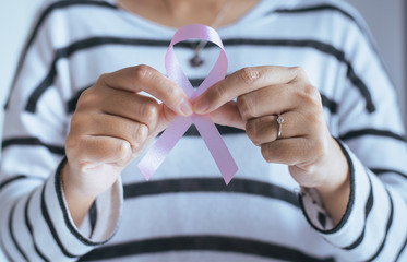 Woman hand holding pink ribbon of breast cancer struggle symbol