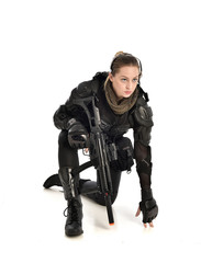 full length portrait of female wearing black  tactical armour, crouching pose holding a weapon, isolated on white studio background.