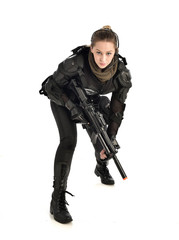 full length portrait of female wearing black  tactical armour, crouching pose holding a weapon, isolated on white studio background.