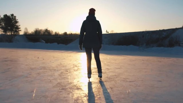 CLOSE UP, LOW ANGLE VIEW: Happy woman iceskating fast on frozen pond in local park at golden sunset on magical Christmas evening. People on ice skates enjoying winter activities in nature, having fun.