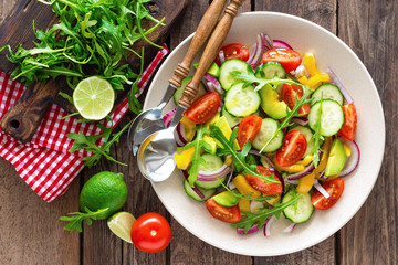 Healthy vegetarian dish, vegetable salad with fresh tomato, cucumber, bell pepper, red onion, avocado and arugula