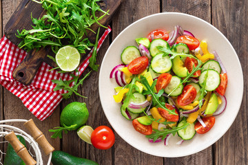 Fototapeta na wymiar Healthy vegetarian dish, vegetable salad with fresh tomato, cucumber, bell pepper, red onion, avocado and arugula