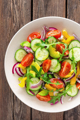 Healthy vegetarian dish, vegetable salad with fresh tomato, cucumber, bell pepper, red onion, avocado and arugula