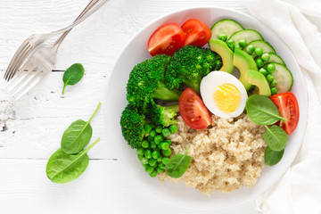 Healthy detox dish with egg, avocado, quinoa, spinach, fresh tomato, green peas and broccoli on white wooden background, top view