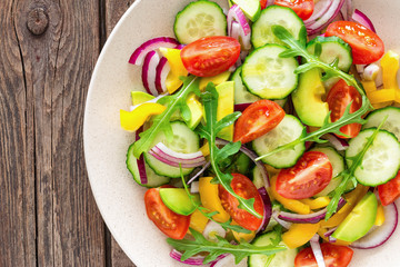 Healthy vegetarian dish, vegetable salad with fresh tomato, cucumber, bell pepper, red onion, avocado and arugula