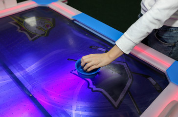 Girl is playing air hockey game and holding striker. Mallets and puck in hands. Violet table with...