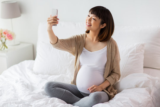 pregnant woman taking selfie by smartphone at home