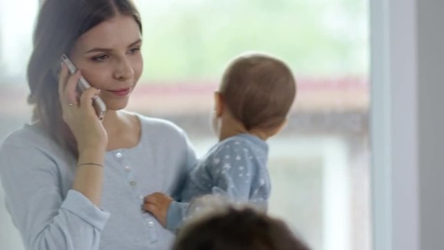 Mother holding baby, cleaning its face and kissing it while talking on the phone