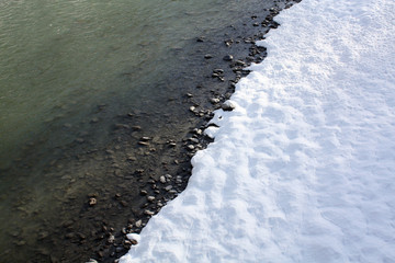 Snow on the river coast in winter in Alps