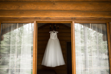 White lush wedding dress hanging on the hanger in the room view from the street. Bridal gown.