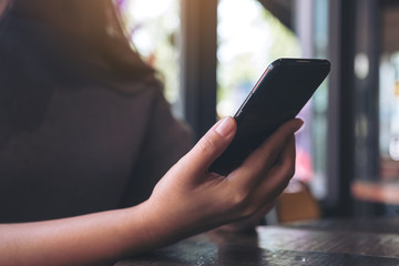 Closeup image of a hand holding and using a black smart phone in cafe
