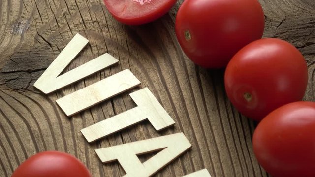 Tomato with inscription VITAMIN on brown wooden surface background. Inscription vitamin and vegetables.