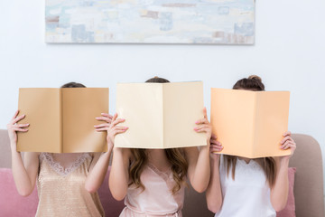 three young women in pajamas hiding faces behind magazines with blank covers