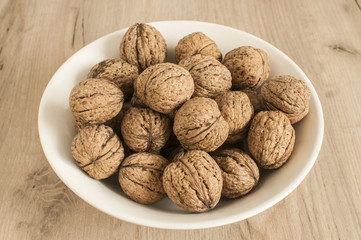 A pile of whole orgranic walnuts in shell closeup in porcelain bowl