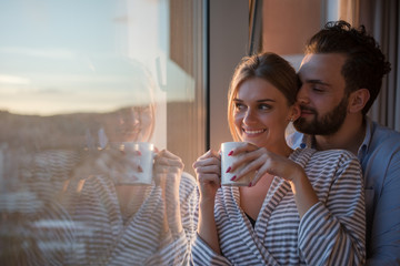 young couple enjoying evening coffee by the window - obrazy, fototapety, plakaty