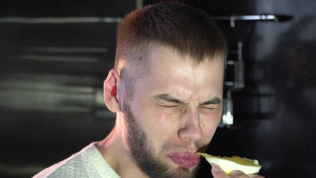 a man eats a juicy lemon wrinkling his face, sour