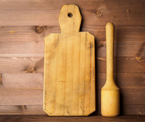 Wooden pestle and rustic old cutting Board on brown dark wooden background. The concept with pounder for menu, recipes