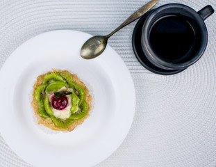 A clay black cup with coffee and a cake on a white plate.