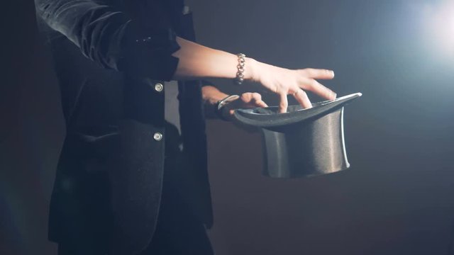 Illusionist is making slow passes over his hat and making impression of taking out an item.