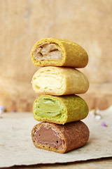 Close up of pile of eclairs in a cut with different filling (chocolate, vanila, coffee, pistachio) over wooden backgroud.