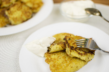 Fried potato pancakes on a white plate and sour cream.