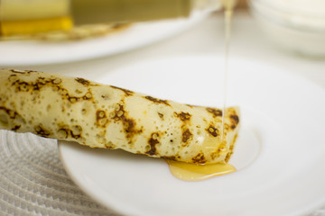 Pancake wrapped in a straw on a white plate watered with syrup.