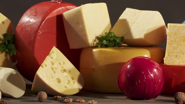 Cheese varieties. Different types of cheeses on wooden table. Stack of cheese wheels, balls and wedges on a dark background. Dolly shot