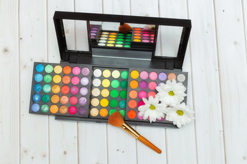 set of multi-colored eye shadow for make-up and make-up brush on a light wooden background
