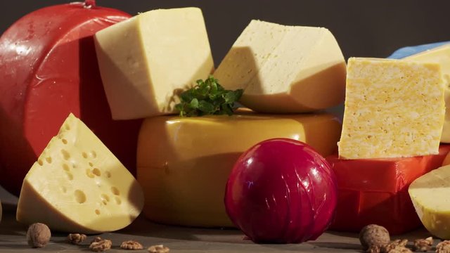 Cheese varieties. Different types of cheeses on wooden table. Stack of cheese wheels, balls and wedges on a dark background. Dolly shot