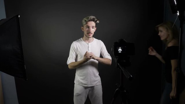 Young smiling vlogger man shooting for his vlog in a professional studio while girlfriend passes through the frame photobomb