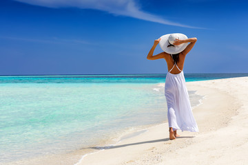 Elegante Frau in weiß läuft über einen tropischen Strand und genießt ihren Urlaub