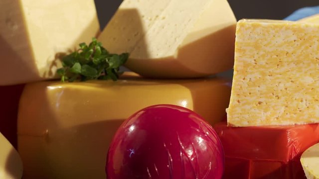 Cheese varieties. Different types of cheeses on wooden table. Stack of cheese wheels, balls and wedges on a dark background. Dolly shot