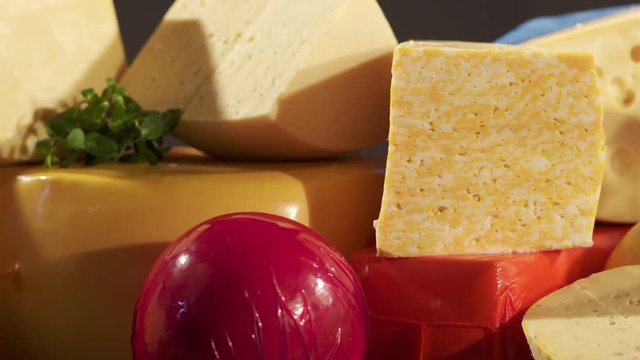 Cheese varieties. Different types of cheeses on wooden table. Stack of cheese wheels, balls and wedges on a dark background. Dolly shot