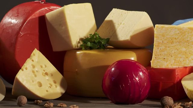 Cheese varieties. Different types of cheeses on wooden table. Stack of cheese wheels, balls and wedges on a dark background. Dolly shot