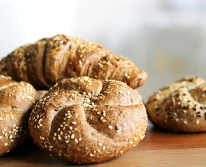Tasty freshly baked butter kaiser roll with linseed and sunflower seeds. Top view, copy space, selective focus. Pastries on a wooden table. Blurred background. Concept of fresh pastry.