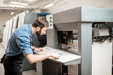 Printing operator working with offset machine at the printing manufacturing
