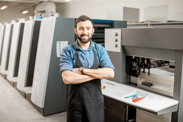 Portrait of a handsome typographer standing at the printing manufacturing with offset machine on...